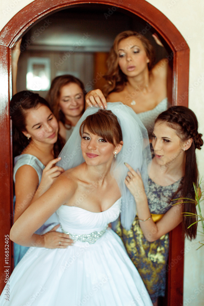 Obraz premium Bridesmaids play with bride's veil while standing in the door