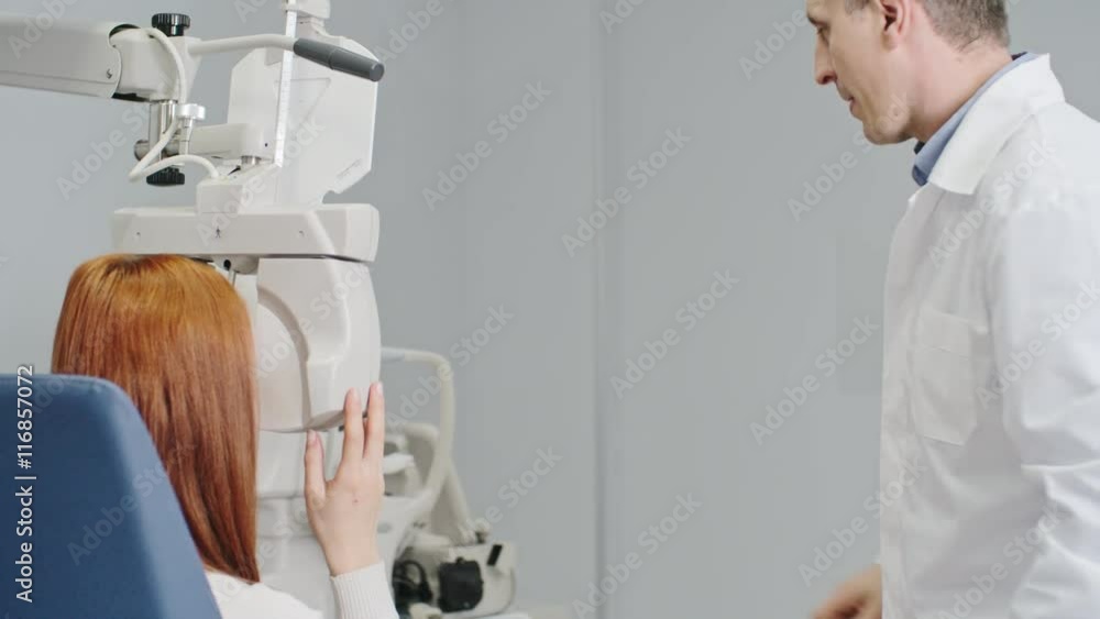 Optometrist using modern equipment to test visual acuity of female patient, woman reading eye chart through digital phoropter Optometrist using modern equipment to test visual acuity of female patient, woman reading eye chart through digital phoropter