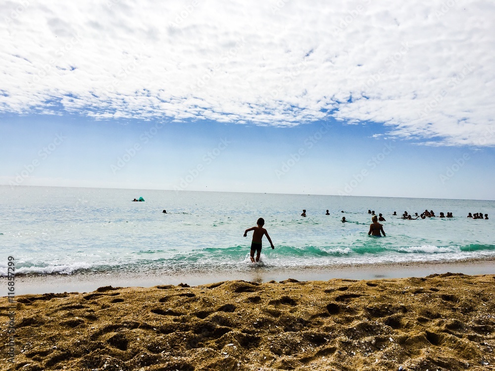 Fototapeta premium Piaszczysta plaża i delikatne fale na morzu, młoda osoba wchodzi do wody