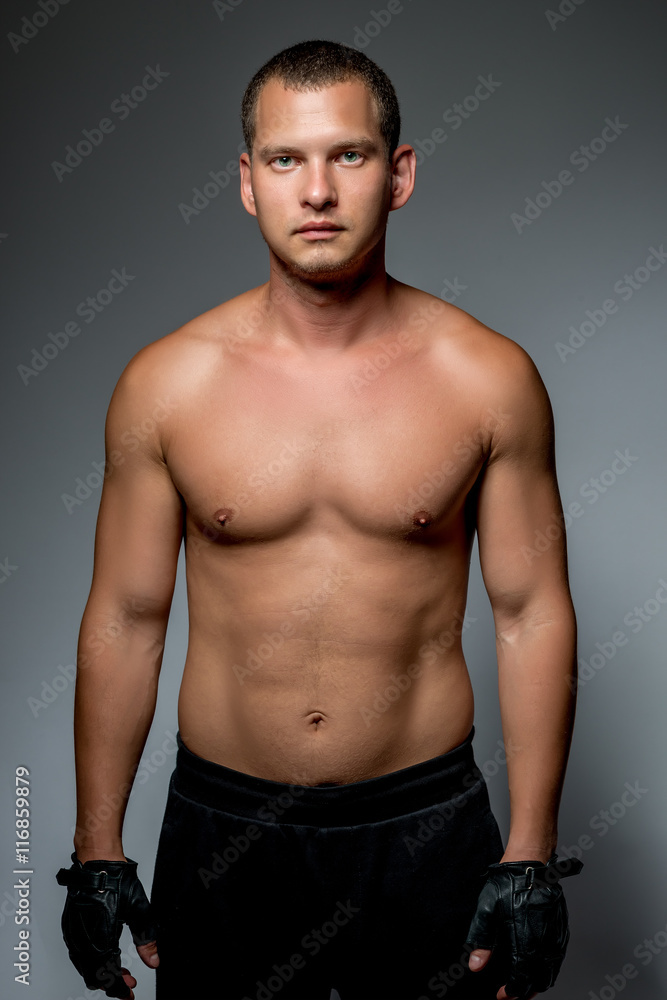 Vertical portrait of a sports man with a naked torso on a gray b Vertical portrait of a sports man with a naked torso on a gray b
