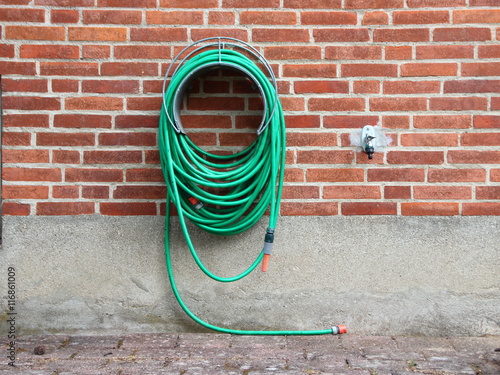 Green Garden Water Hose mounted on Red Brickwall