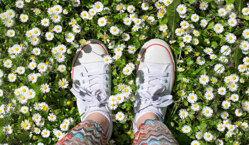 White sneakers in a dasiy field. woman walking