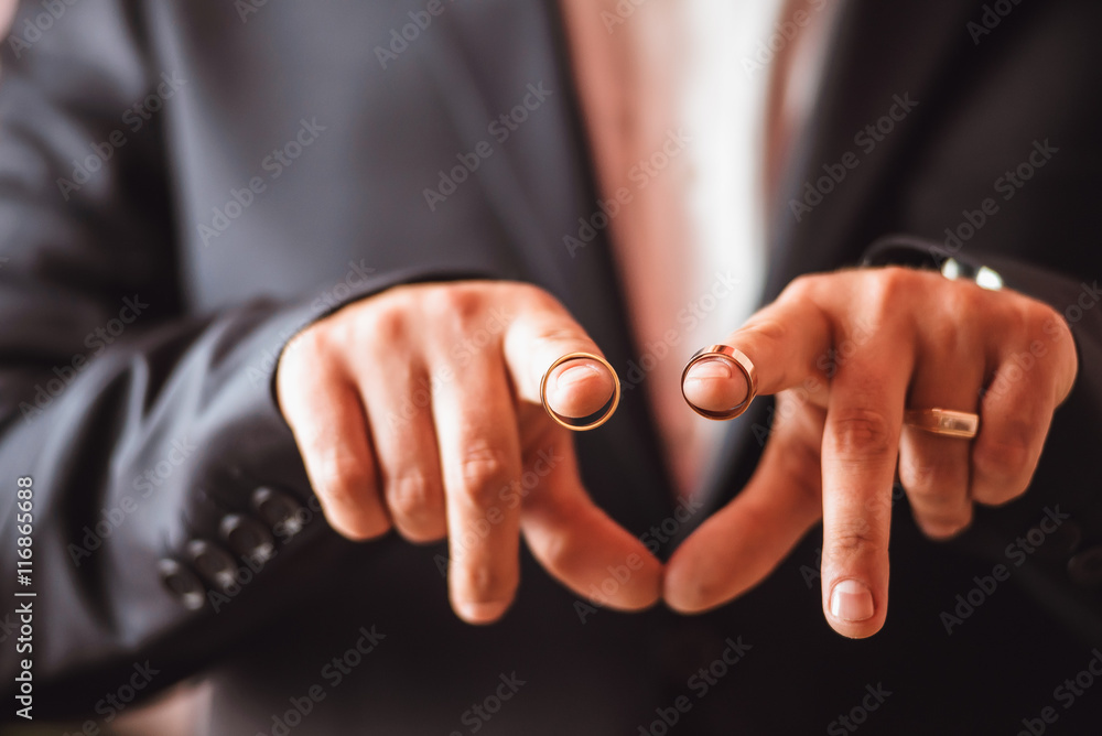 Closeup of a groom holding gold wedding rings
