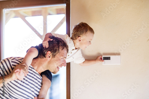 Father carrying son on shoulders, adjusting thermostat photo