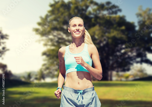 smiling young woman running or jogging over park