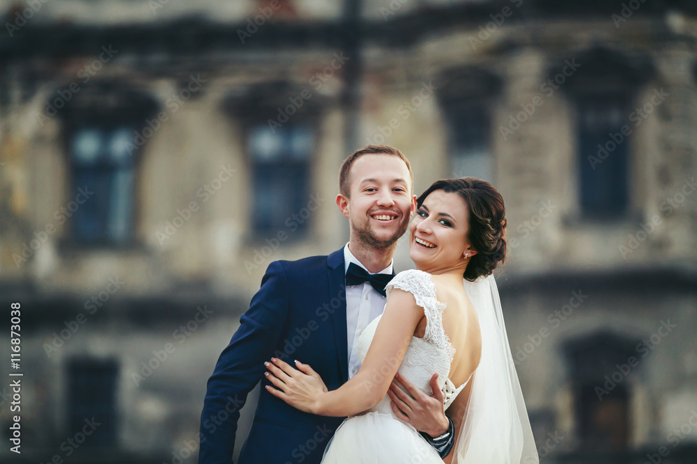 Fototapeta premium Smiling newlyweds hug in the front of an old castle
