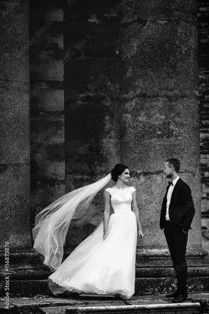 Wind blows bride's veil while she stands with a groom between th