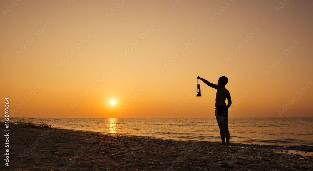 Young boy with lamp at sunrise on the beach