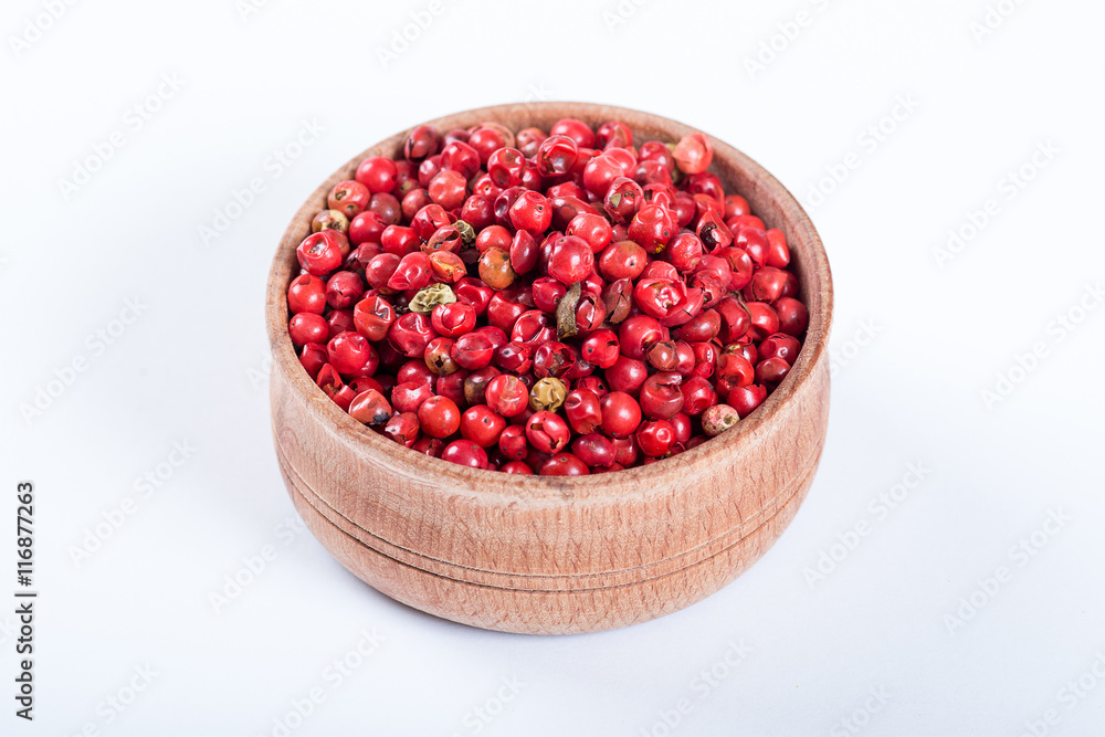 Pink pepper in a wooden bowl isolated on white background Pink pepper in a wooden bowl isolated on white background