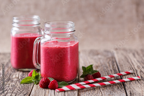 Tasty raspberry smoothie in glass jar on wooden table.