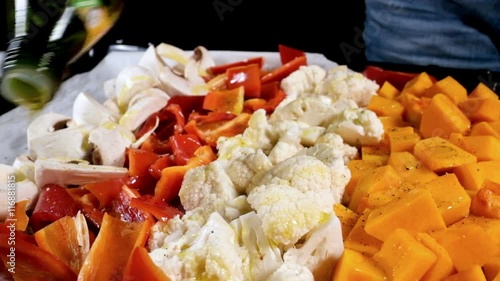 A cook pours olive oil on chopped vegetables on a frying pan photo