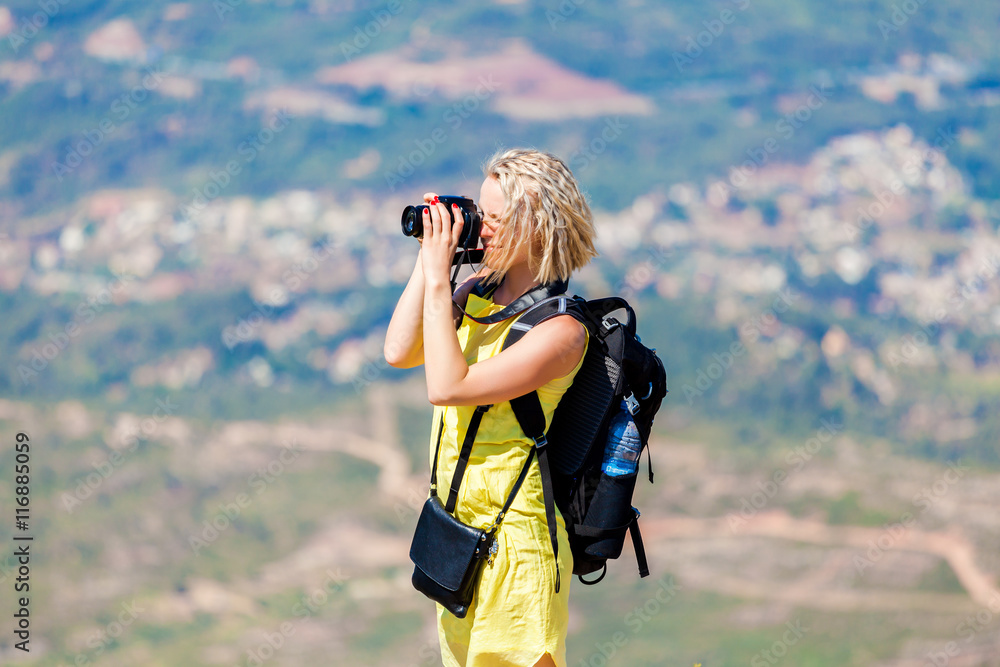 Female traveler stands on a hill and looks over the valley bottom and takes pictures. Woman enjoying the views from the top of the mountain and make a photo.