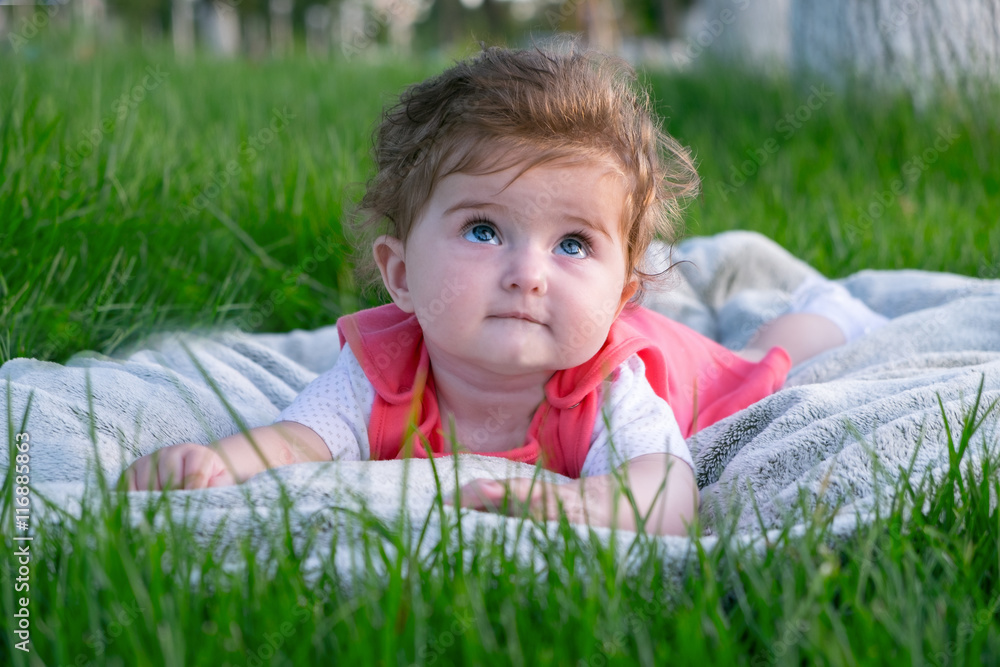 Little girl (six months old) with beautiful blue eyes is lying on the grass in the park. She looks up. Little girl (six months old) with beautiful blue eyes is lying on the grass in the park. She looks up.