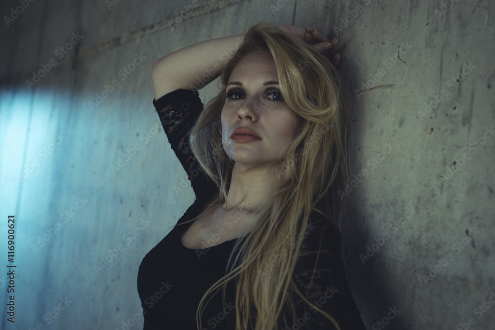 Fototapeta premium Posing, blonde dressed in skintight black costume on a gray ceme