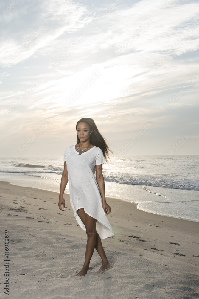 Beautiful African American female model posing on beach in white dress Beautiful African American female model posing on beach in white dress