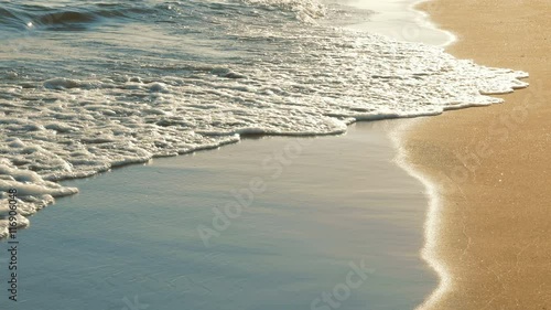 Close up of surf with soft sea waves rushing on sandy beach on sunset with sun reflection. Enjoying summer vacation on tropical country. Nature background