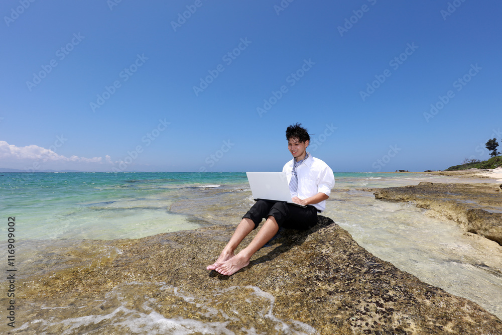 美しいビーチでパソコンを楽しむ笑顔の男性