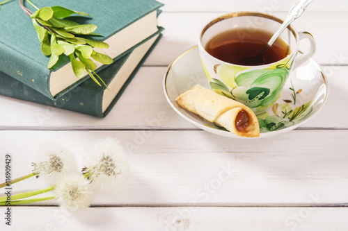 Cup of tea, cookies, stack of books and dandelions on a white wooden background 