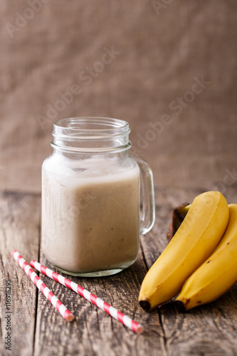 Healthy banana smoothie in glass jar with bananas on wooden tabl