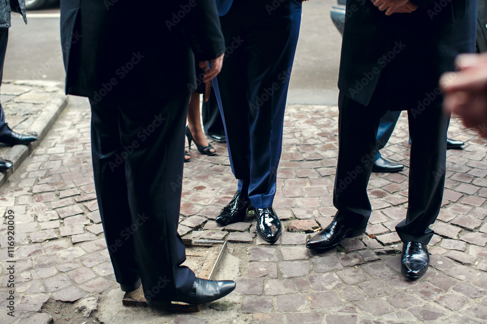 Men in suits stand on the  pavement outdoors