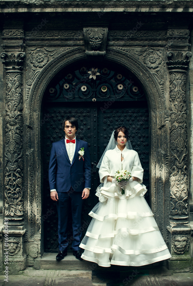 Bride and groom stand straight behind an old steel door