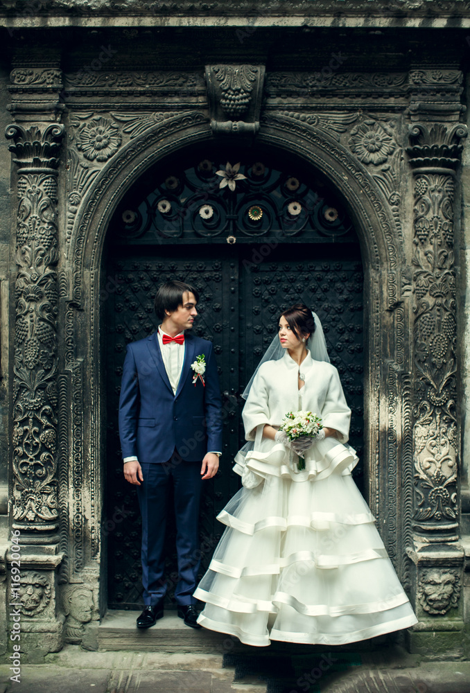 Newlyweds look at each other standing behind an old steel door