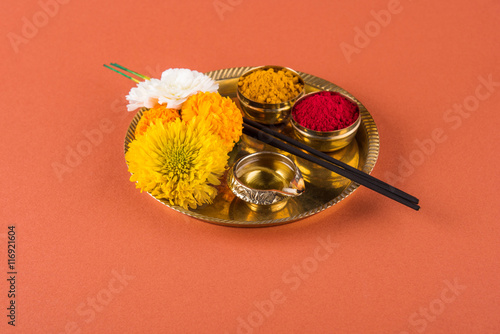 Beautifully Decorated Pooja Thali for diwali celebration to worship, huldi or turmeric powder and kumkum, flowers, scented sticks in brass plate on orange background, hindu puja thali