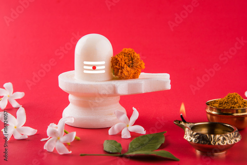 Shiva Linga made up of white marble decorated with flowers & bael leaf known as Aegle marmelos, over white background, maha shiva ratri a festival of hindu God shankar or shankar bhagwan or bholenath