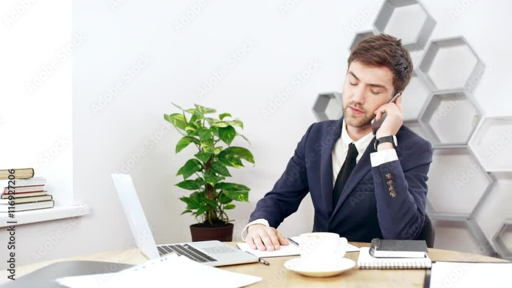 Young successful businessman speaking on phone at his workplace in office. Slow motion.