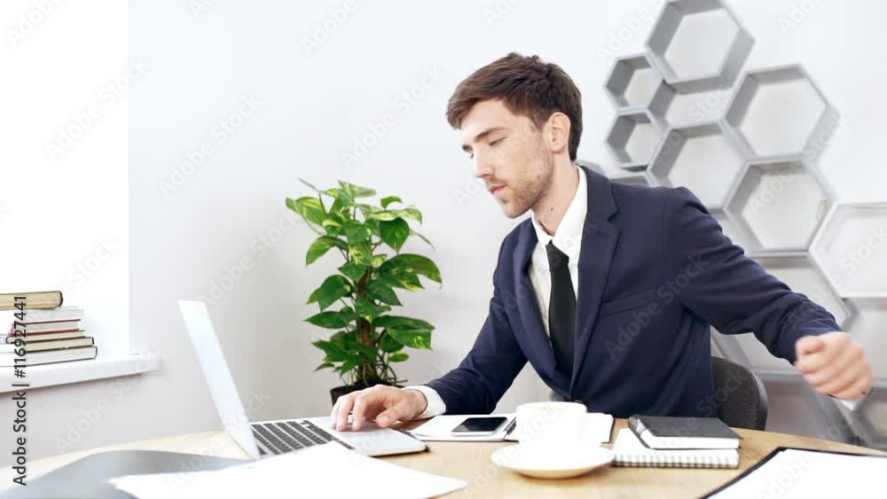 Young successful businessman working at laptop in office. Slow motion.