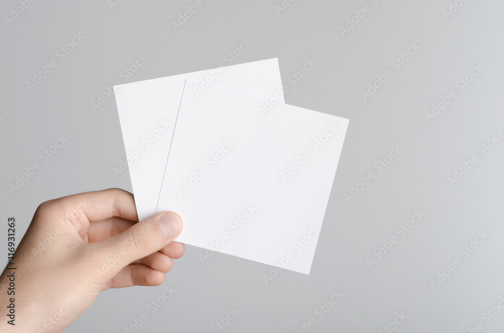 Fototapeta premium Square Flyer / Invitation Mock-Up - Male hands holding blank flyers on a gray background.