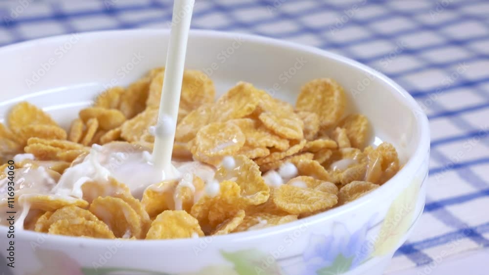 Breakfast cereal pouring milk with splashes into bowl of golden corn flakes in slow motion Breakfast cereal pouring milk with splashes into bowl of golden corn flakes in slow motion