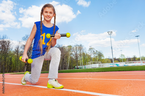 Active girl doing exercises with dumbbells outdoor