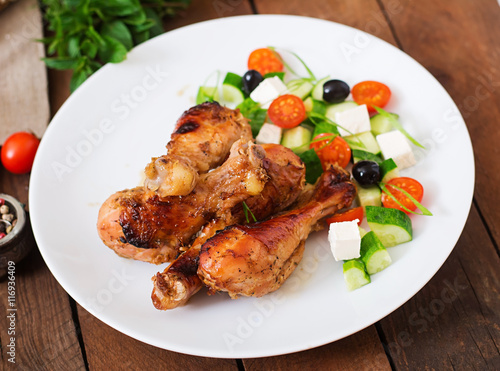 Appetizing oven baked golden chicken drumsticks and Greek salad