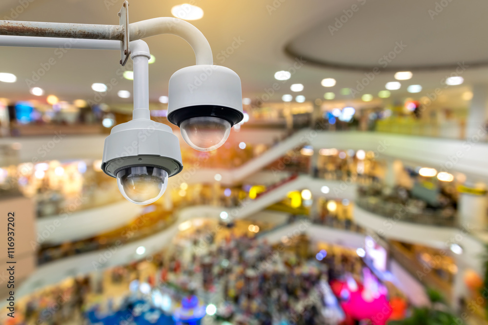 Closeup CCTV security camera on blurred inside shopping mall