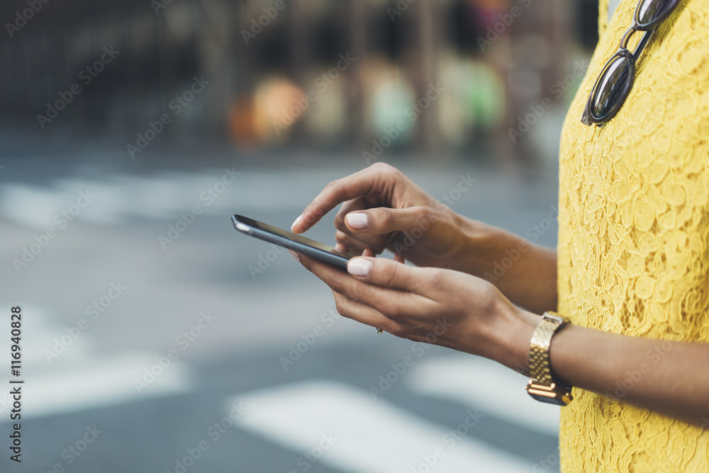Close-up image of female hands using modern smart phone outside, woman’s hands typing on touch screen of cellphone while standing at crosswalk in the city