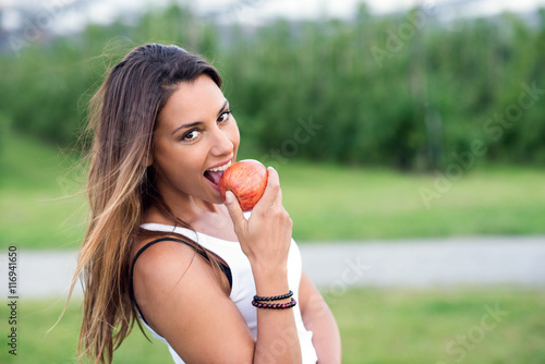 Junge Frau beisst in einen gesunden Apfel und lacht glücklich dabei
