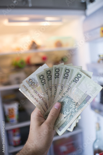 hand with PLN  money in front of open fridge
