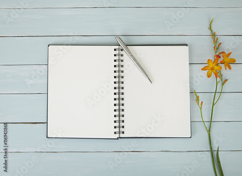 A journal open on a blank page, with flowers and a pen on a blue wooden desktop background