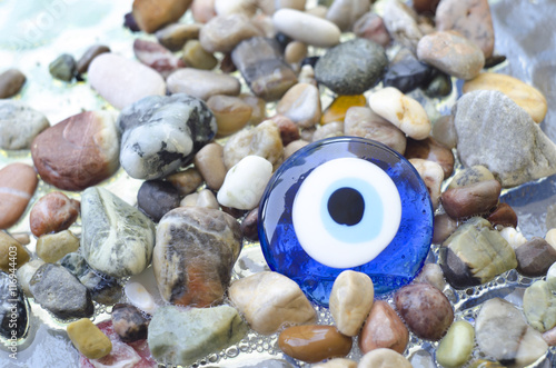 Colorful pebbles on the beach with turkish evil eye glass bead. Background with color stones on the sea and amulet photo