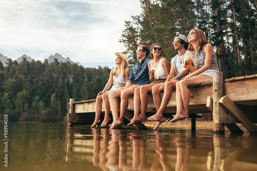 Group of friends sitting on jetty at lake