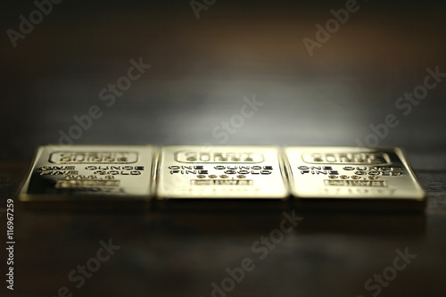 three 1 ounce gold ingots on wooden background
