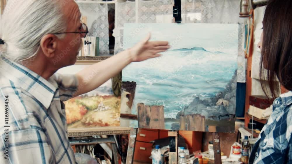Pair of male and female skilled artists discussing a finished painting in art studio Pair of male and female skilled artists discussing a finished painting in art studio