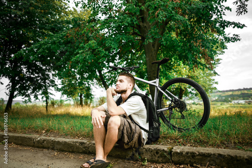 Man sitting beside the road with his bike and resting photo