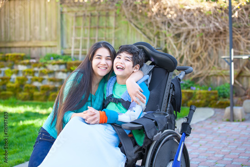 Teenage girl hugging disabled brother in wheelchair outdoors