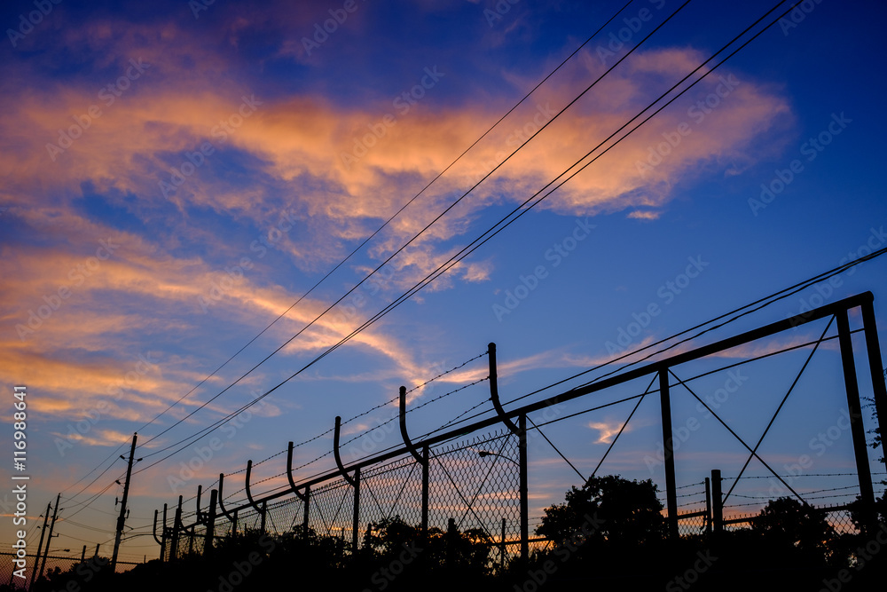 Electrical power line and fence in sunset or sunrise