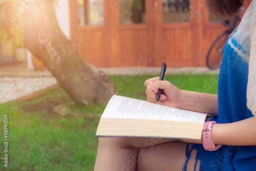 Young woman reading and mark something on book sitting in garden