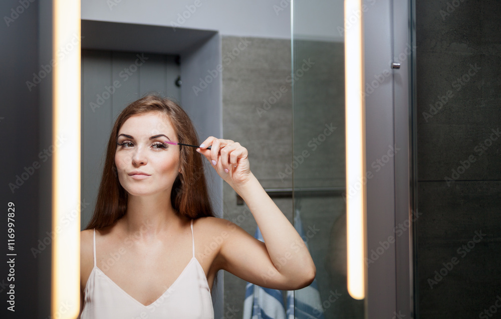 Woman applying mascara on long eyelashes in front of mirror Woman applying mascara on long eyelashes in front of mirror