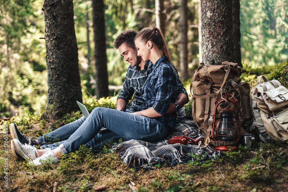 A couple of tourists sitting and looking at laptop in the woods. The concept of active rest A couple of tourists sitting and looking at laptop in the woods. The concept of active rest