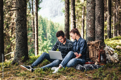 A couple of tourists sitting and looking at laptop in the woods. The concept of active rest